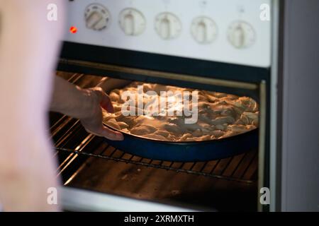 Elderly woman putting pie in the oven Stock Photo