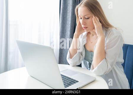 Stressed business woman working at home on laptop with headache feeling frustrated, bored and tired. Female with challenges of remote work, feelings Stock Photo