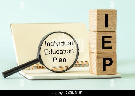 Individual Education Plan IEP symbol. Business concept, IEP 504 program, text on natural wooden block placed next to open school notebook and magnifyi Stock Photo