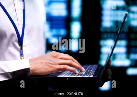 IT specialist in front of server clusters performing data backups, close up. Manager using laptop to make sure electric generators are able to ensure operational continuity Stock Photo
