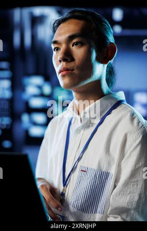 IT developer in data center uses laptop to prevent system overload during peak traffic periods. Trained specialist in server room ensuring enough network bandwidth for smooth operations Stock Photo