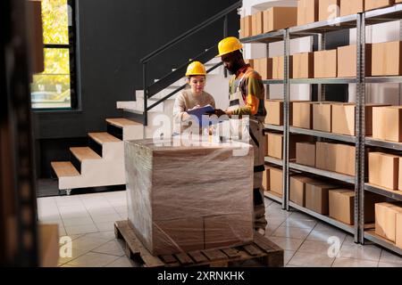 Diverse warehouse coworkers analyzing customers orders document, preparing packages for shipping using cardboard boxes in storage room. African american team working in storehouse Stock Photo
