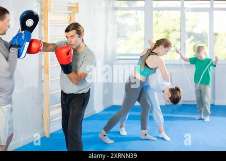 Focused man in boxing gloves practices punches with man in mitts in gym Stock Photo