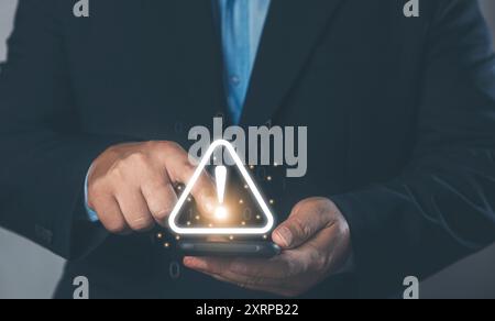 Warning alerts and antivirus system software detection. A businessman is holding a smartphone with a cautionary warning sign for notification errors a Stock Photo
