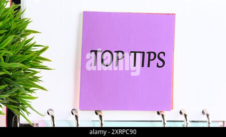 top tips word. text concept symbol TOP TIPS on a purple sticker on the background of a blank sheet of a business book Stock Photo