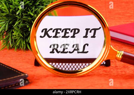 Conceptual symbol. Copy space. Keep it real words written through a magnifying glass on a white business card on an orange background Stock Photo