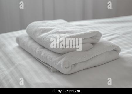 Folded clean white towels on hotel apartment bed, selective focus Stock Photo