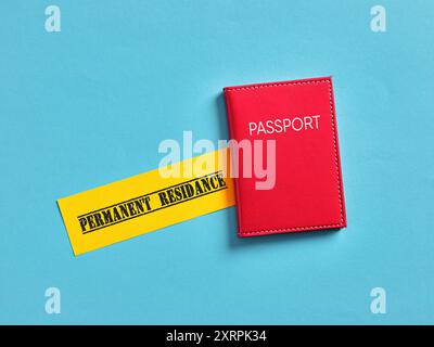 Red passport lying near permanent residence sign over blue background is suggesting immigration and citizenship concept. Stock Photo