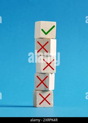 Making the right decision after wrong ones. Stack of wooden cubes is showing one right choice against many wrong ones over a blue background. Stock Photo