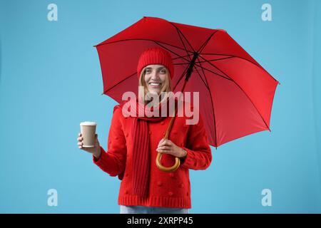 Woman with red umbrella and paper cup on light blue background Stock Photo