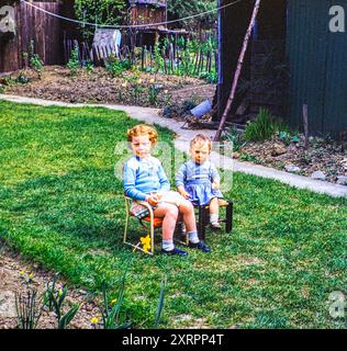 Little girl with ginger hair and toddler sitting on small chairs on lawn in back garden, UK 1956 Stock Photo