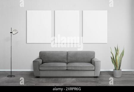 Three art canvases in a living room with sofa, plant, and lamp. White clean canvas surfaces for mockup art presentation and home decor showcase Stock Photo