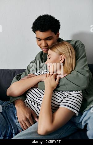 A young multicultural couple enjoys a tender moment of intimacy, embracing on a couch in their modern apartment. Stock Photo