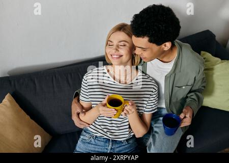 A young interracial couple enjoys coffee together on a comfortable couch in a modern apartment. Stock Photo