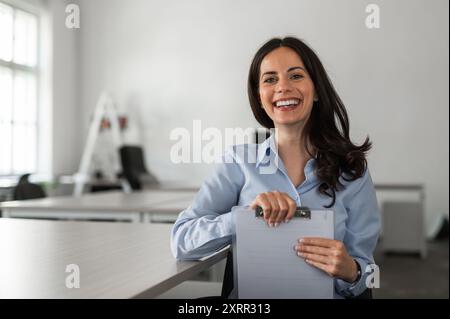 Young and cheerful employee at her desk holding documents Stock Photo