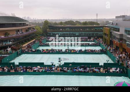 Spectators sitting in the rain on outside courts  at the 2024 Wimbledon Championships,London,England. Stock Photo