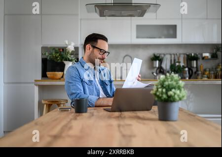 Young entrepreneur with laptop on desk analyzing financial report while working from home office Stock Photo