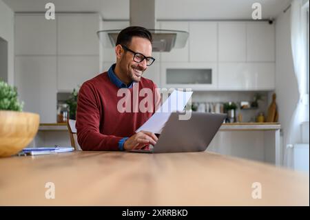 Happy male financial adviser reading income tax form and working over laptop on desk in home office Stock Photo