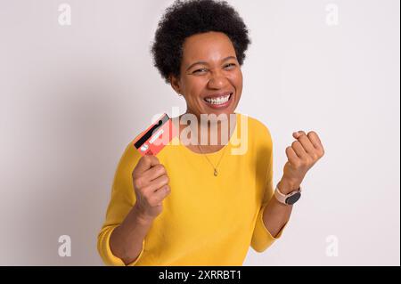 Excited young woman holding credit card and pumping fist while standing over white background Stock Photo