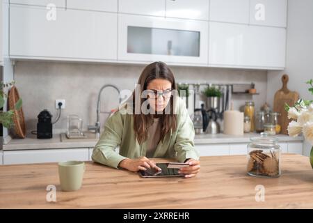 Young confused woman holding credit card looking on digital tablet screen having issue with online banking or shopping, credit card limit and overspen Stock Photo