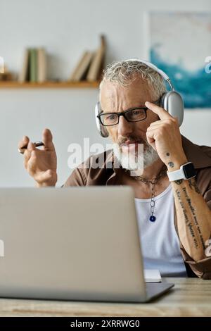 A mature gay man with tattoos and grey hair works remotely from home. Stock Photo