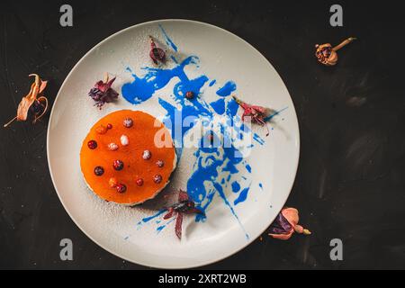 Dessert with sea buckthorn and orange mango jelly with cottage cheese and chocolate with blue curacao sauce on a white plate with flowers on a black b Stock Photo
