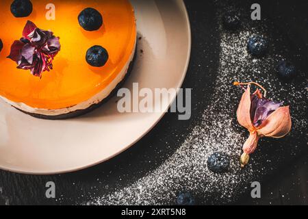 Dessert or cake with layers of chocolate, curd cream, mango jelly, decorated with food dried flowers on a white plate on a black background. Original Stock Photo