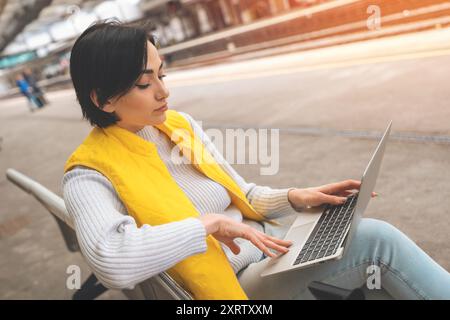 woman at railway station using computer, laptop while waiting train.  Working, studying, shopping, booking online. Enjoying travel concept. Stock Photo