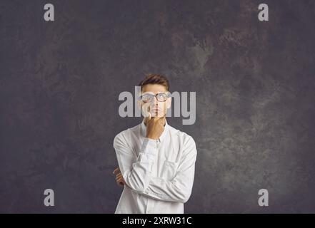 Young man with hand on his chin who is thinking about question with pensive expression. Stock Photo