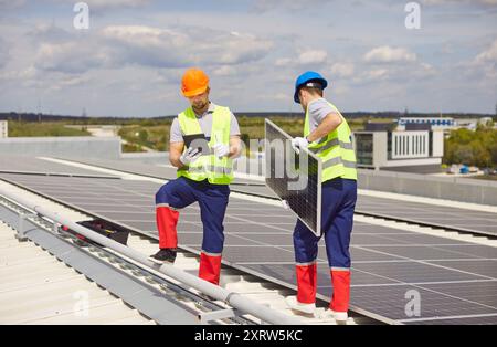 Repairmen are maintaining and installing solar panels on a rooftop. Stock Photo