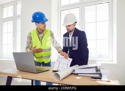 Two male contractors in hard hats discuss the master plan in a room Stock Photo