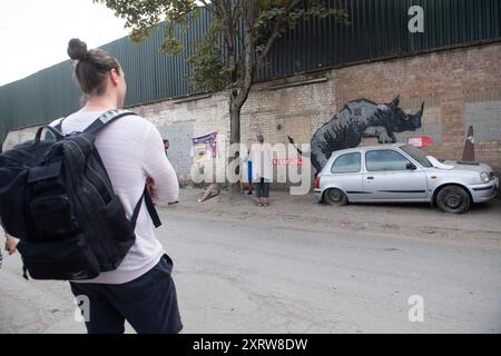 London, UK. 12 Aug 2024. People pose for photos with Street Artist Bansky's Eighth new mural depicting a rhino mating with a 1990s model Nissan Micra car made to look like a rhino in Charlton. Credit: Justin Ng/Alamy Live News Stock Photo