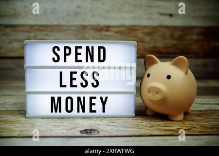 Spend Less Money text on LED lightbox with piggy saving on wooden background, Money concept Stock Photo