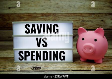 Saving VS Spending text on LED lightbox with piggy saving on wooden background Stock Photo