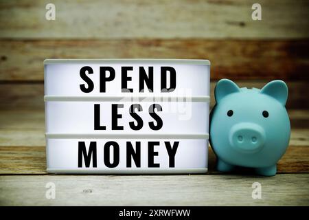 Spend Less Money text on LED lightbox with piggy saving on wooden background, Money concept Stock Photo