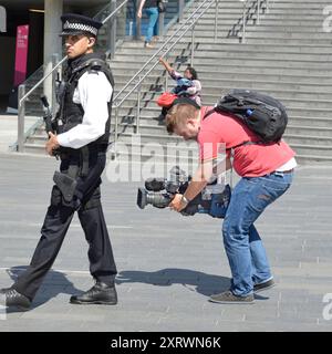 Cameraman with large camera seemingly filming back view close up of armed Metropolitan police officer on patrol London 2012 Olympic Games Stratford UK Stock Photo