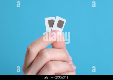 Woman holding SIM cards on light blue background, closeup Stock Photo
