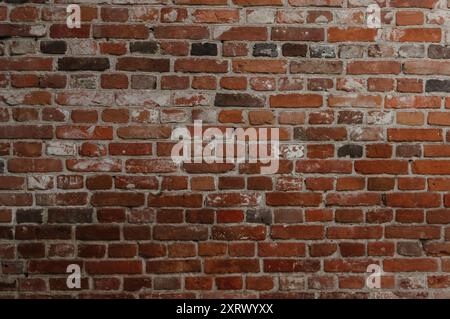 A brick wall with a few missing bricks. The wall is red and has a rough texture. The wall appears to be old and has some wear and tear Stock Photo