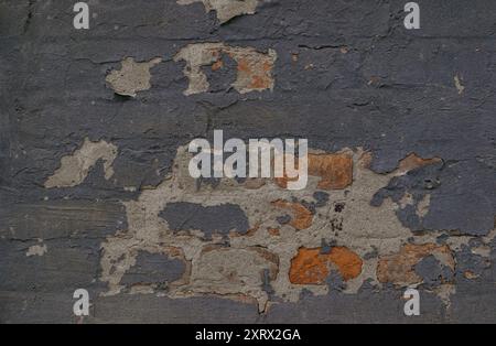 A brick wall with a few holes and cracks. The wall is gray and has a few brown bricks Stock Photo