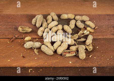 Peanuts in the shell with a few broken shells lying on a rough wood table Stock Photo