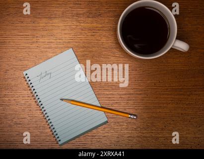 White coffee cup on wooden counter with black coffee and note pad showing start of today list Stock Photo