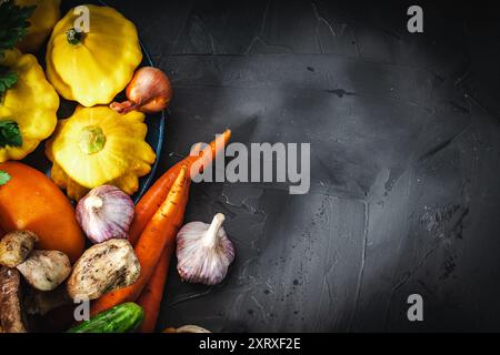 Autumn and summer vegetables and mushrooms on a black background. Small yellow pumpkins, carrots, tomatoes and cucumbers, garlic, onions. Seasonal veg Stock Photo