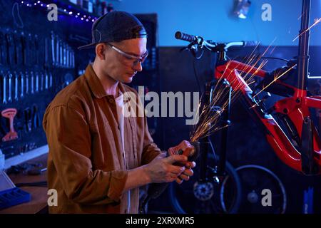 Young handsome man bike mechanic using circular saw for repair work Stock Photo