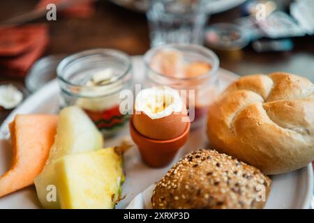 Boiled Egg Cracked Open on a Breakfast Plate with Bread Buns and Fruit Slices Stock Photo