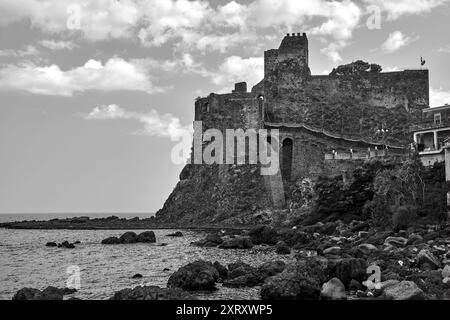 Ruins of a Norman castle on a volcanic cliff in the village of Aci Castello on the island of Sicily, Italy,  monochrome Stock Photo