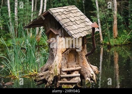 Charming wooden house built into a tree stump, located on a pond in a lush forest, evoking a fairytale atmosphere.  Stock Photo