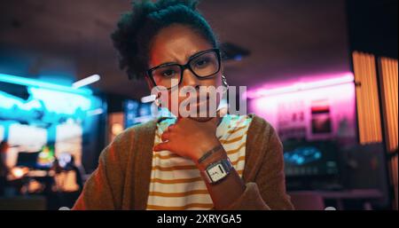 Stylish Young Black Woman Looking at Camera With Confusion While Working on Desktop Computer in Creative Office. Female Developer Trying to Fix a Bug, Unsure of the Source of the Issue Stock Photo