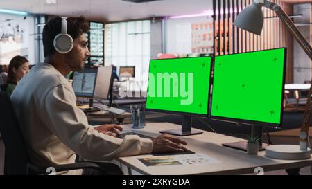 Indian Male Game Designer Using Desktop Computer With Green Screen Chromakey on Display, Designing Immersive World In 3D modelling Software For RPG Video Game. Man Working In Game Development Office Stock Photo
