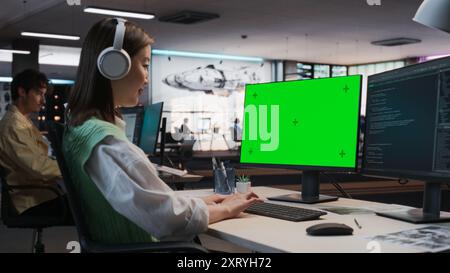 Female Asian Game Programmer Coding On Desktop Computer With Green Screen Chromakey On Display In Game Development Studio Office. Focused Woman Does Gameplay Engineering For New 3D RPG Video Game. Stock Photo