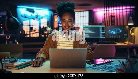 Portrait of a Black Smiling Female, Using Laptop Computer, Smiling in a Creative Office. Empowered Information Technology Specialist and Developer Working on a Project Stock Photo